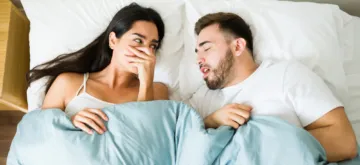 bad breath - Couple in bed on valentines day with the female in the image covering her nose due to the bad breath of her partner