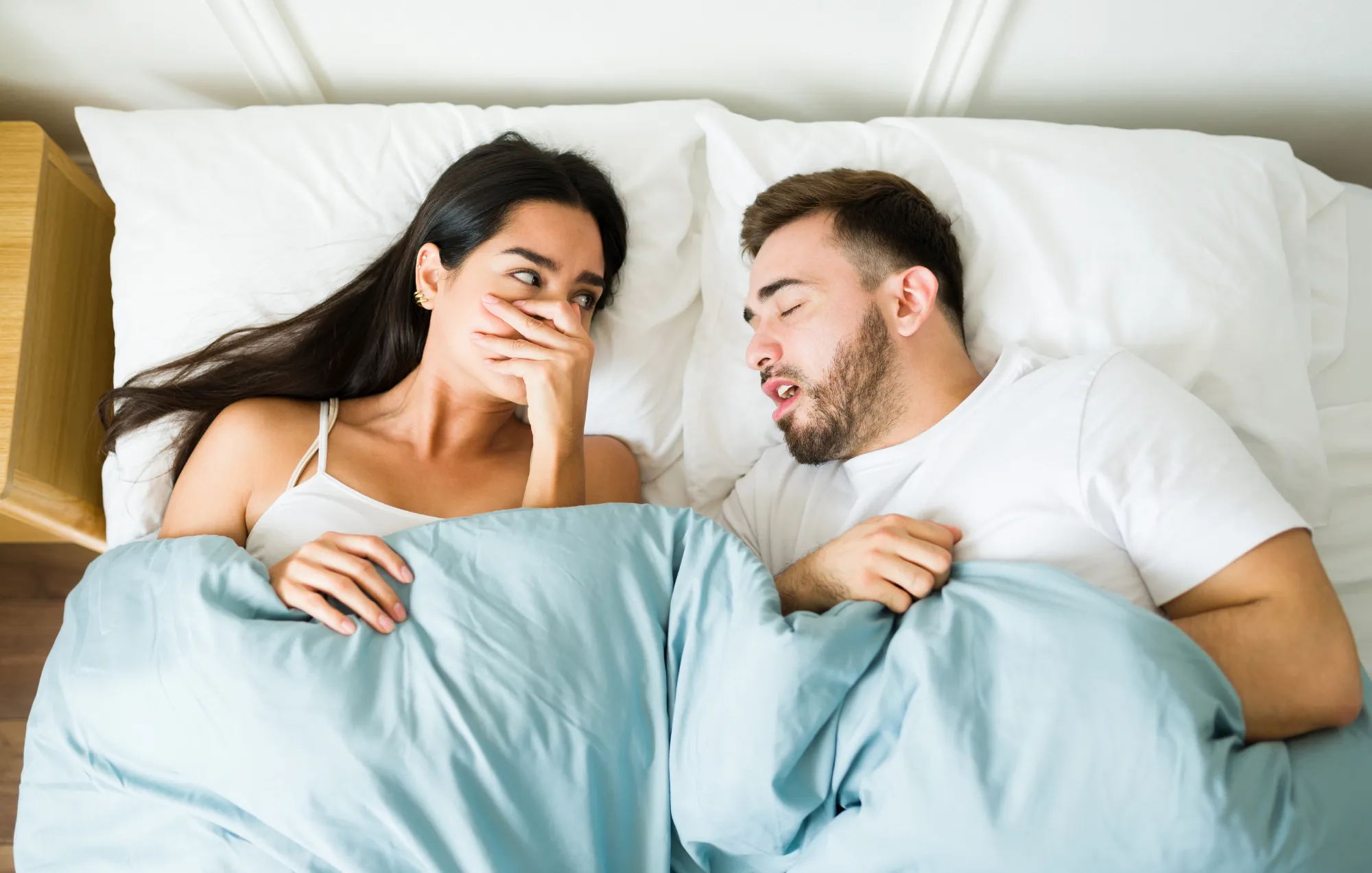 bad breath - Couple in bed on valentines day with the female in the image covering her nose due to the bad breath of her partner