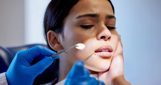 Nervous woman holds cheek during dental exam, dentist in blue gloves.