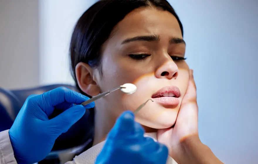 Nervous woman holds cheek during dental exam, dentist in blue gloves.